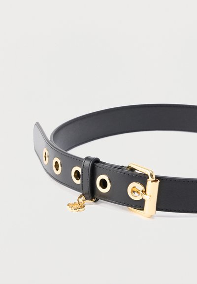 Μαύρη δερμάτινη ζώνη με λεία υφή, διακοσμημένη με χρυσά χαντράκια και χρυσή αγκράφα. Περιλαμβάνει ένα μικρό διακοσμητικό γούρι που είναι προσαρτημένο.