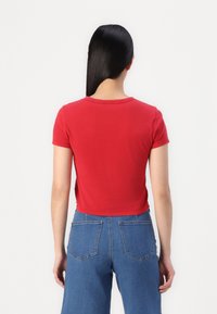 Rode, korte mouw, crop top gemaakt van katoen. Gladde textuur met een ronde halslijn. Gecombineerd met blauwe denim, hoge taille broek.