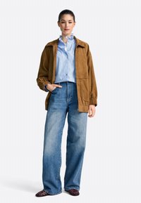 Brown suede jacket with elastic cuffs, light blue striped shirt, high-waisted wide-leg jeans, and burgundy woven shoes.