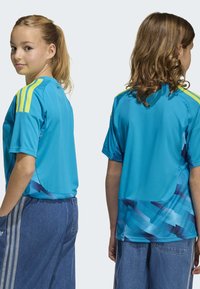 Blå atletisk tröja med korta ärmar, med gula accenter på axlarna och ett mönstrat blått nedre parti. Mjukt, lättviktigt tyg.