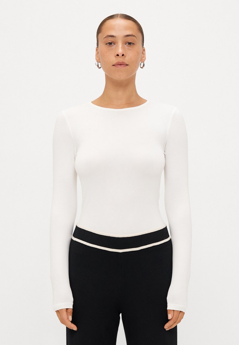 Top bianco a maniche lunghe realizzato in tessuto leggero, con scollatura rotonda e fit slim, abbinato a pantaloni neri con cintura a contrasto.