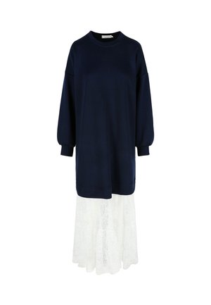 Námornícky svetrový šaty s dlhými rukávmi a okrúhlym výstrihom, preložené cez bielu krajkovú sukňu s kvetinovými vzormi a splývavým lemom.