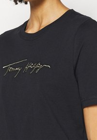 Zwarte katoenen t-shirt met een gouden geborduurd merkteken, met een ronde halslijn en korte mouwen, een gladde textuur en een eenvoudig ontwerp.