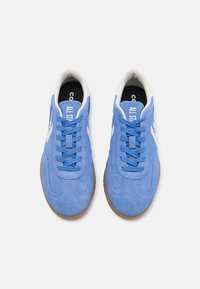 Adidași din suede albastru cu accente și șireturi albe, având un material superior texturat și o talpă din cauciuc brun, etichetați "ALL STAR" pe limbă.