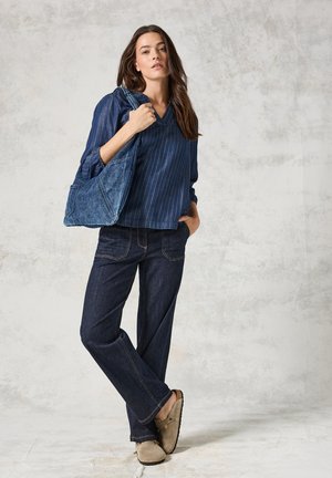 Navy gestreepte blouse met V-hals, losse pasvorm, gecombineerd met donkere denim flared jeans en beige instap schoenen. Een blauwe denim tas maakt de look compleet.