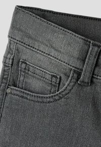 Gros plan sur la zone de la poche d'un jean en denim noir montrant la poche principale, une petite poche pour la monnaie, une passants de ceinture et un détail de rivet métallique.