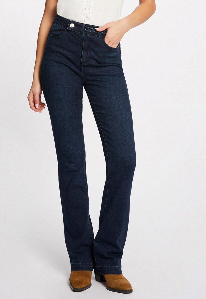 Jean flare bleu foncé avec une taille haute, dotés de poches cousues et d'un bouton décoratif. Le tissu a une texture lisse et légèrement extensible.