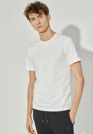 Biała bawełniana koszulka z okrągłym dekoltem, krótkimi rękawami i dopasowanym krojem. Posiada delikatne logo na rękawie.