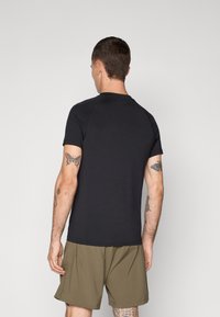 T-shirt de sport noir à manches courtes avec un col rond, texture lisse et couture contrastante. Porté avec un short vert olive.
