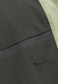 Sportovní top Nike s tmavě zelenými a světle zelenými sekcemi, hladkým povrchem, horizontálním černým pruhem a vyšitým logem.