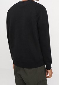 Sudadera negra con cuello redondo acanalado y mangas largas tipo raglán. La tela parece suave con una textura lisa y un dobladillo ajustado.