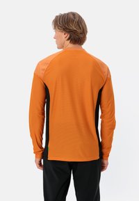 Langärmliges Sporthemd mit einem orangen Körper, schwarzen Seiten und kontrastierenden Schulterpaneelen. Verfügt über einen strukturierten Stoff und ein grünes Akzentetikett.