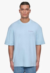 Lys blå oversized t-skjorte laget av bomull, med rund hals og korte ermer; liten "Dropsize" logo brodert på brystet.