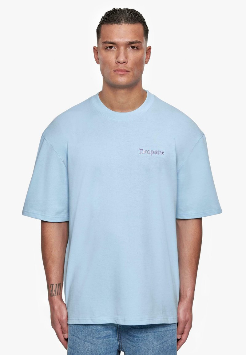 Lys blå oversized t-skjorte laget av bomull, med rund hals og korte ermer; liten "Dropsize" logo brodert på brystet.