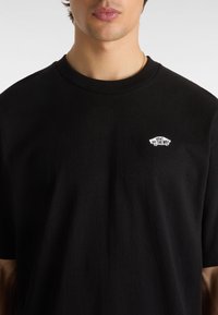 T-shirt in cotone nero con collo rotondo e maniche corte. Piccolo logo bianco "Vans Off The Wall" sul lato sinistro del petto. Texture liscia.