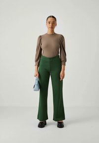 Beige ribbet topp med puffete ermer, parret med høyt liv grønne vide bukser. Holder en lyseblå veske, iført svarte klumpete sko.