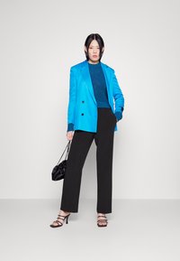 Blazer azul brilhante ajustado, suéter texturizado azul, calças largas pretas, bolsa preta e sapatos de salto pretos com tiras.