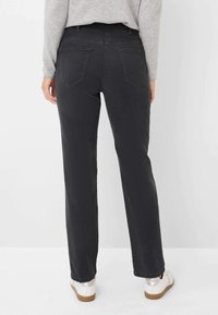 Zwarte denim broek met een recht model, twee achterzakken en lichte vervagingdetails, gedragen met witte schoenen en een grijze top.