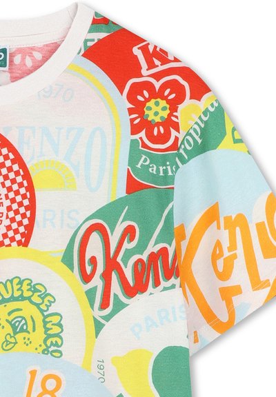 T-shirt en coton avec un imprimé graphique coloré comprenant divers motifs circulaires, incluant du texte et des motifs floraux en rouge, vert et jaune.