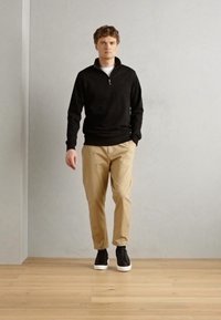 Black zip-up sweater, beige chinos, and black sneakers with white soles. Simple design, tailored fit, and lightweight fabric textures.