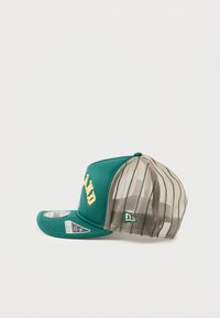 Zelena kapa s čvrstim prednjim dijelom, žutom izvezenom logom i mrežastim stražnjim dijelom s tankim vertikalnim prugama. Uključuje zakrivljeni vizir i detalj s logom sa strane.