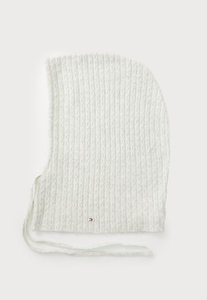 Hvit strikket hette med et teksturert mønster. Har bånd ved halsen og en liten metallisk detalj. Myk, fleksibel stoff med en buet form.