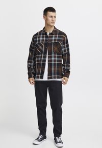 Brun og blå rutete flanellskjorte med to brystlommer, knappelukking, båret over en hvit t-skjorte; kombinert med svarte bukser og sneakers.