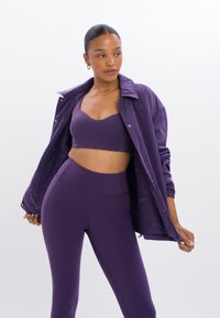 Paarse sportoutfit met een aansluitende beha, high-waisted leggings en een lichtgewicht, knoopsluiting jack met ribbelmanchetten.