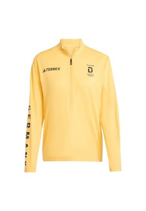 Żółty długi rękaw z krótkim zamkiem. Na przodzie czarne logo Adidas, napis „TEAM” oraz symbole olimpijskie. Na rękawie wyraźny napis „GERMANY”.