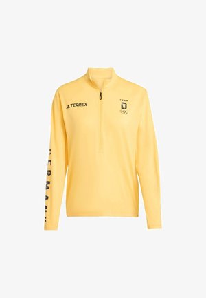 Żółty długi rękaw z krótkim zamkiem. Na przodzie czarne logo Adidas, napis „TEAM” oraz symbole olimpijskie. Na rękawie wyraźny napis „GERMANY”.