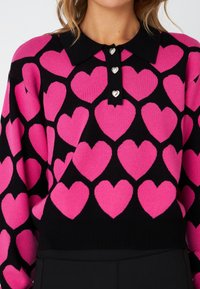 Maglione lavorato a maglia con base nera e grandi motivi a cuore rosa, colletto nero e tre bottoni a forma di cuore in argento.