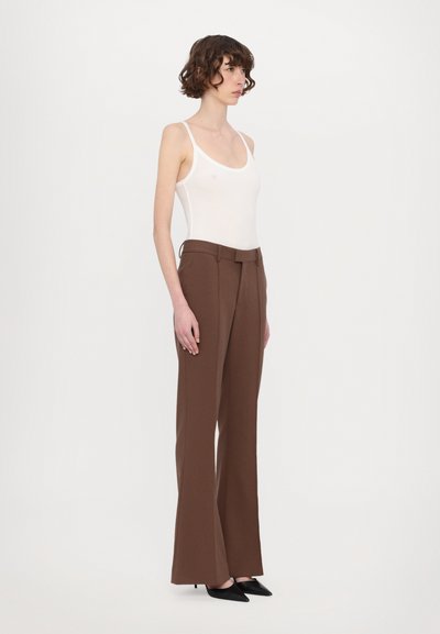 Pantalons marron ajustés avec une coupe droite, taille haute et passants de ceinture, associés à un haut près du corps blanc et des escarpins noirs à bout pointu.