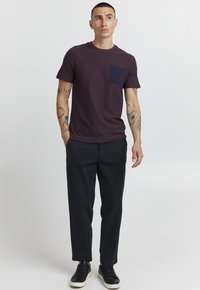 T-shirt à rayures marron avec une poche avant bleu foncé, associée à un pantalon noir et des baskets noires. Le tissu semble doux et confortable.