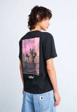 T-shirt in cotone nero con una grafica sul retro di una creatura su uno sfondo di tramonto rosa. Il design include testo e dettagli.