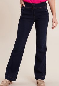 Pantaloni flare in denim blu scuro, a vita alta con dettagli a bottoni sulle tasche. Cuciture a contrasto e una texture liscia, aderenti sui fianchi.
