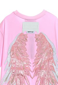 Camiseta rosa con un gran diseño de alas de ángel metálicas en color plata y rosa en la parte posterior, con una etiqueta rectangular cerca del escote.