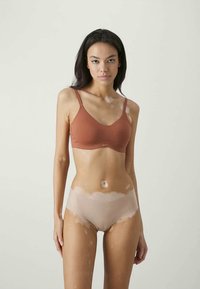 Smeđa oblikovana bralette s podesivim naramenicama, u kombinaciji s svijetlo bež bešavnim hipster gaćicama; oboje napravljeno od rastezljive, meke tkanine.