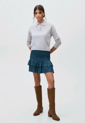 Siv pritej džemper, teal nabran krilo s polka pikami in rjave suede škornje do kolen. Preprost dizajn z mehkimi teksturami in plastičnim stilom.
