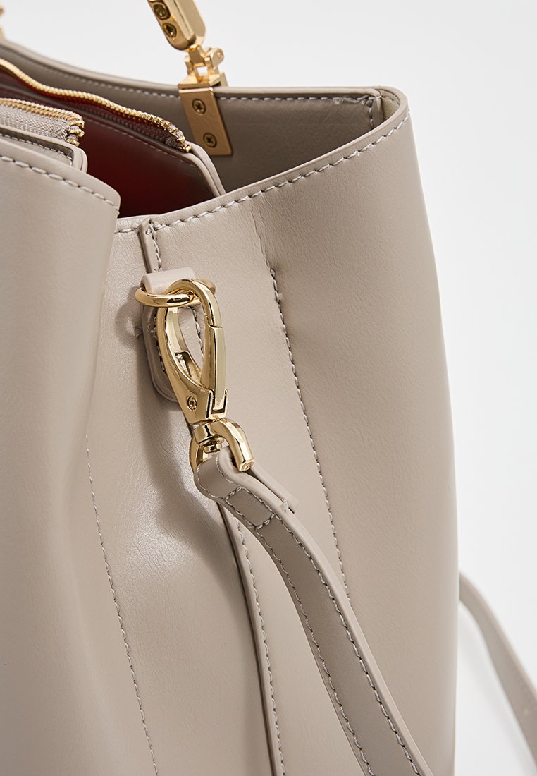 Sac à main en cuir beige avec des accessoires en métal doré, doté d'une fermeture zippée sur le dessus, d'une surface texturée et d'une bandoulière amovible pour plus de polyvalence.