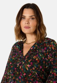 Blusa nera a fiori con modelli multicolori vivaci, design a V, e sottili dettagli di cucitura. Tessuto morbido con una caduta fluida.