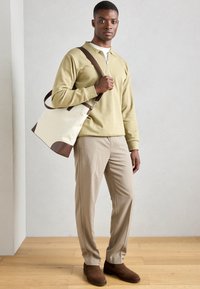 Beige bolyhos pulóver cipzáros gallérral, bézs kosztümnadrág és barna bokacsizma. Kézben egy krémszínű vászontáska barna kiegészítőkkel.