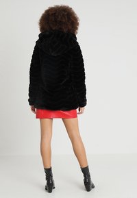 Musta tekoturkistakki, jossa siksak-kuvio ja huppu, yhdistetty punaiseen nahkaseelikseen ja mustiin nilkkureihin, joissa korko.