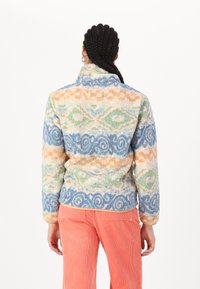 Fleece pullover met hoge kraag, multicolore geometrische patronen in pastelkleuren zoals blauw, groen, oranje en roze. Zachte textuur.