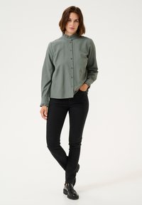 Light green button-up shirt with a ruffled collar and cuffs, paired with black slim-fit pants and glossy black shoes. Simple and tailored design.