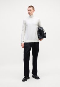 Heledhall hallide turtleneck-sviiter, mustad püksid ja must kott. Sviiter on figuuri järgi lõigatud; kangas näeb välja pehme. Jalatsid on mustad, suurte tallaga.