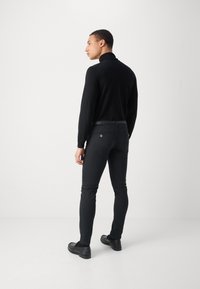 Maglietta nera a maniche lunghe e pantaloni neri aderenti, che mettono in risalto un tessuto liscio, un design minimalista e un discreto dettaglio della tasca posteriore. Scarpe nere completano il look.