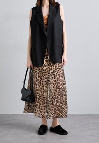 Svart ärmlös väst över en brun och svart leopardmönstrad kjol; svart crossbody-väska; svarta, fluffiga slip-on-skor.