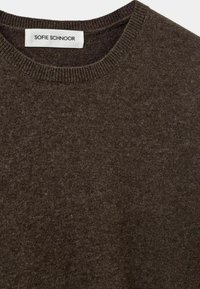 Brown knitted sweater featuring a ribbed crew neckline. Soft texture with a subtle pattern. Label reads "SOFIE SCHNOOR."