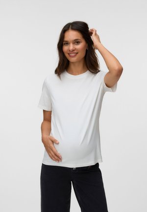 Lächelnde schwangere Frau im weißen T-Shirt und schwarzen Hosen hält mit einer Hand ihren Bauch und berührt mit der anderen ihr Haar vor einfarbigem Hintergrund.