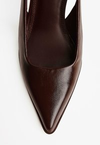 Pointed-toe shoe in dark brown leather. Features a smooth texture and cut-out sides. Slip-on design with no visible hardware or accents.